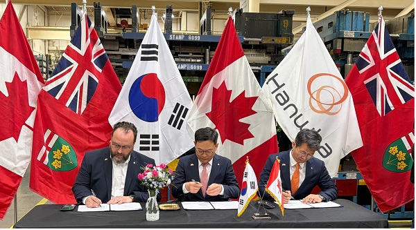 Three men sign documents at a table during an international signing ceremony, with multiple national flags in the background.