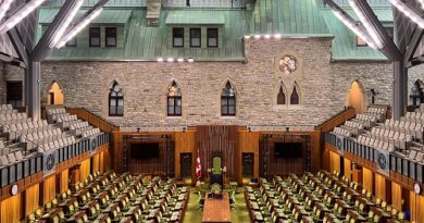 Empty parliamentary chamber with green seats, a central podium, Canadian flag, and stone walls in a historic hall.