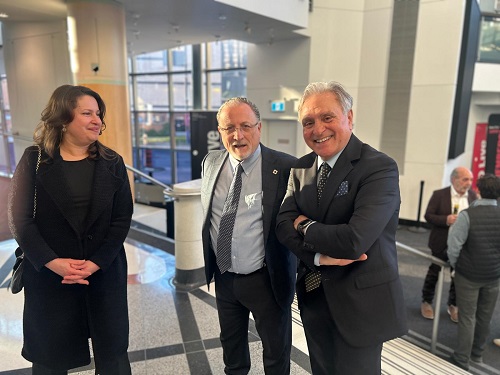 Three people in business attire smile at the camera in a bright, modern lobby.