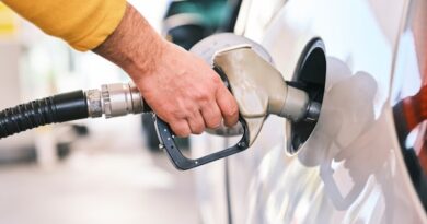 Person refueling a car at a gas station, gripping a fuel nozzle near the fuel tank cap on the car's side