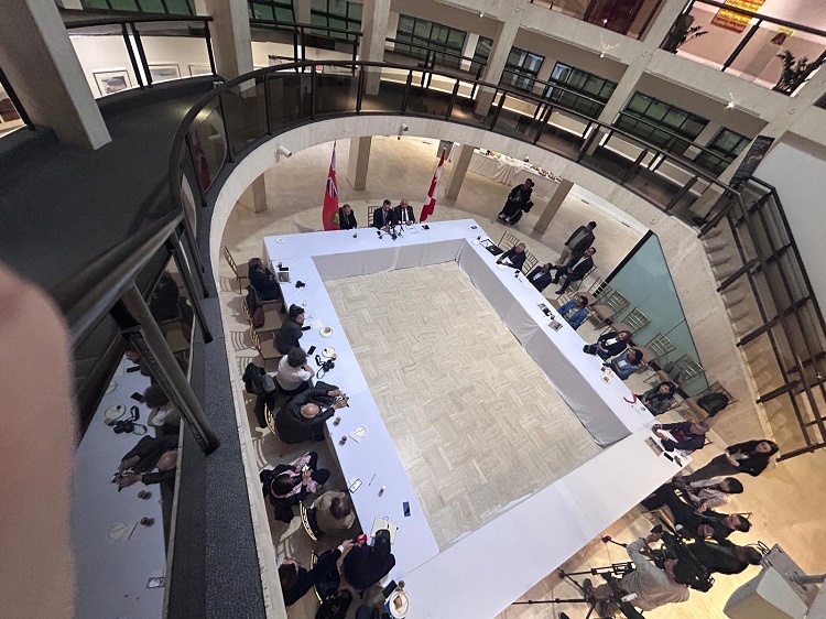 Overhead view of a U-shaped conference table in a circular atrium, with attendees around and flags nearby.