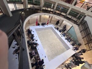 Overhead view of a U‑shaped conference table in a circular atrium, with attendees seated around and flags behind the head table.