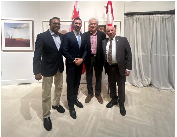 Four men in suits posing for a group photo at an indoor event, two shaking hands, with Canadian flags and artwork visible in the background.