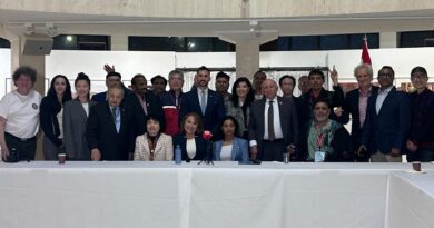 Group of diverse officials and attendees posing for a conference photo behind a long white table with microphones, flags on either side.