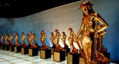 Row of identical gold-toned statues standing on black pedestals along a wall in a museum or gallery exhibit.