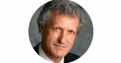 Circular headshot of a middle-aged man with gray hair in a dark suit.