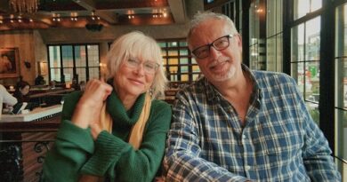 Smiling elderly couple sitting at a cafe table, leaning toward each other with warm lighting in a busy restaurant.
