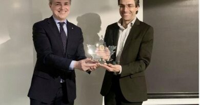 Two men in suits exchange a trophy during a formal event, smiling at the camera.