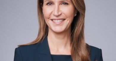 Professional headshot of a smiling woman in a navy blazer against a gray studio backdrop.
