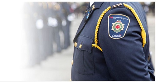 Close-up of a Canadian police officer's dark blue uniform sleeve with crest badge and gold braid, blurred crowd in the background.