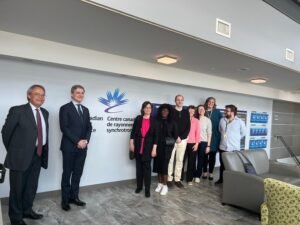 Group of people posing together in a modern lobby outside a wall with the Canadian Centre for Synchrotron Radiation logo and text.