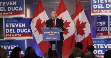 Politician Steven Del Duca giving a campaign speech at a podium with Canadian flags and multiple 'Re-Elect Steven Del Duca for Mayor' signs behind him.