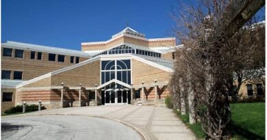 Front view of a large brick campus building with a glass entryway and curved driveway under a clear blue sky.