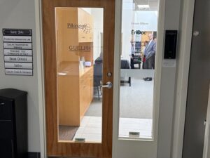 Wood-framed glass door to an office suite; signs read Pilkington and GUELPH on the door, with a person visible inside.