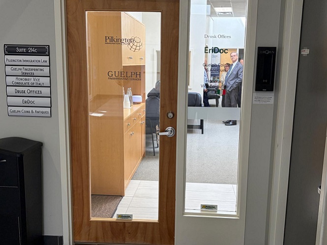 Wood-framed glass door to an office suite; signs read Pilkington and GUELPH on the door, with a person visible inside.