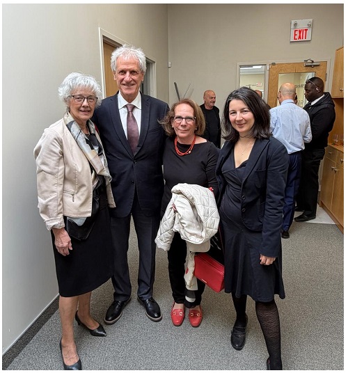 Four professionals posing in a hallway, two women on the left and two on the right, dressed in business attire with coats and a red purse visible in the center.