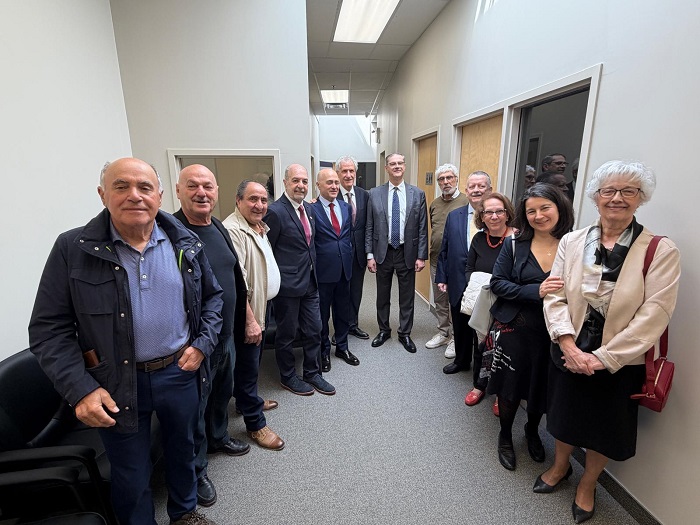 Group of professionals in a narrow office hallway, posing for a photo; most wear suits or smart-casual attire, with a mix of men and women.