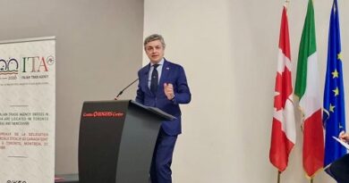 Man in a blue suit speaks at a conference podium on a stage with Swiss, Italian, and EU flags behind him.