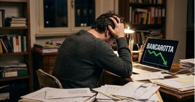 A man sits at a cluttered desk with papers, head in hands, while his laptop shows 'BANCAROTTA' with a green downward arrow.