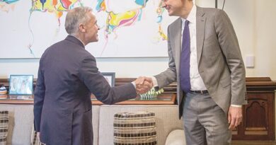 Two businesspeople in suits shake hands in a formal office with a colorful abstract painting in the background.