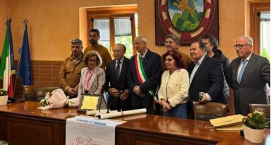 Group of officials posing at a town hall long table, with Italian and EU flags and a banner displayed on the desk.