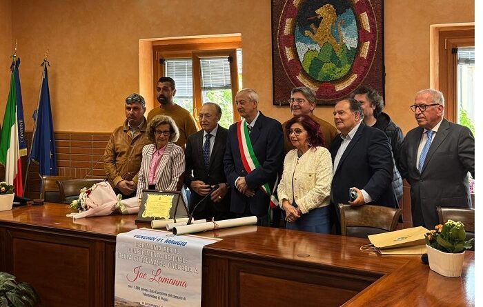 Group of officials posing at a town hall long table, with Italian and EU flags and a banner displayed on the desk.