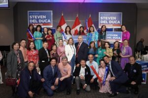 Group of diverse supporters posing at a Steven Del Duca for Mayor campaign event, with campaign signs and Canadian flags in the background. Transitioning to a group portrait style photo with many people smiling.