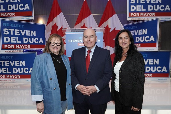 Three adults posing at a campaign event with blue 'Steven Del Duca for Mayor' signs and Canadian flags in the background.