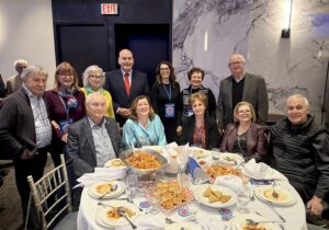 Group of adults posing for a photo around a round banquet table with plates of food and drinks.