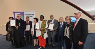 Group of ten people at an awards ceremony posing for a photo, several holding framed certificates, with a banner that says “Nobody’s perfect” in the background.