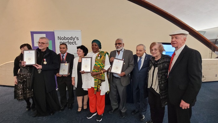 Group of people at an awards ceremony posing with certificates; backdrop features a banner that says "Nobody's perfect".