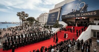 Red carpet arrivals at the Cannes Film Festival outside the venue, with photographers, reporters, and a large festival banner by the sea.