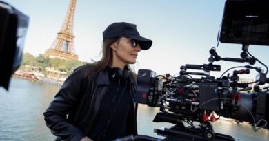 Camera operator on a boat filming with a large rig, Eiffel Tower visible in the background.