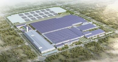 Aerial view of a large industrial campus with extensive blue solar panels on rooftops and a fenced perimeter around the site.