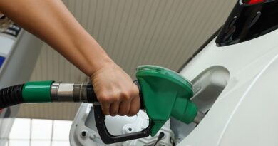 Person refueling a white car with a green fuel nozzle at a gas station.
