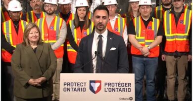 Man in a dark suit speaks at a podium labeled 'Protect Ontario' as workers in hard hats and safety vests stand behind him.