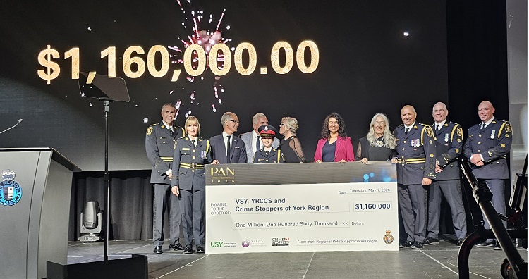 Ceremony on stage presenting a large check for $1,160,000 to Crime Stoppers of York Region, with uniformed officers and officials surrounding the offset check.