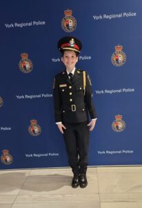 Young girl in police uniform posing in front of a York Regional Police backdrop.