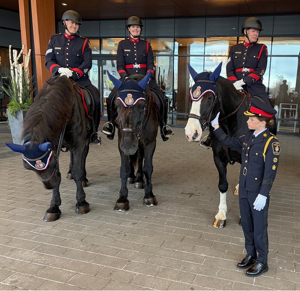 Ceremonial guards on horseback outside a modern building; a young officer stands on the ground beside them.