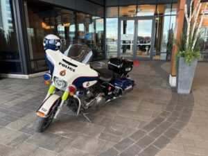 White police motorcycle with blue and red accents parked outside a glass-front building entrance.
