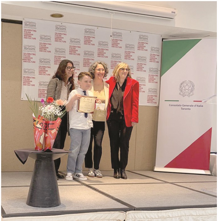 Boy in a white shirt holds a certificate on stage, flanked by three adults; backdrop shows Librissimi logos and an Italian Consulate banner.