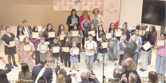 Group of children on a stage holding certificate awards during a ceremony, with a few adults and photographers in the foreground.