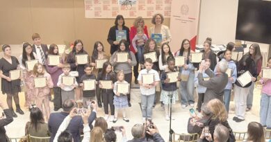 Group of children and teens on a stage holding certificates at an award ceremony, with adults and photographers in the audience.