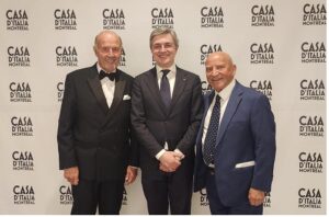 Three men in formal suits posing for a photo in front of a Casa d'Italia Montréal backdrop at an event.