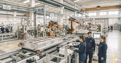 Factory floor with orange robotic arms assembling a large metal frame on a conveyor, while three technicians monitor a control panel.