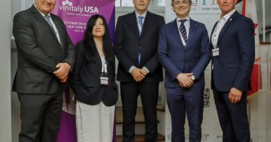 Five professionals in business attire stand in a hallway with Vinitaly USA banners behind them at an event.