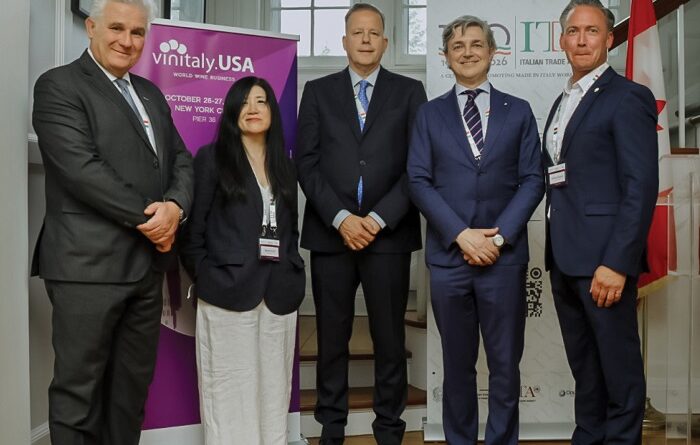 Five professionals in business attire stand in a hallway with Vinitaly USA banners behind them at an event.