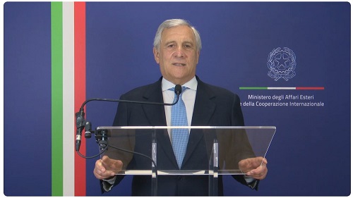 Government official delivering a speech at a podium, with the Italian flag colors and Foreign Affairs Ministry emblem behind.