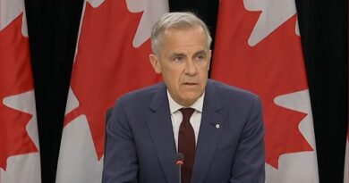 Man in a blue suit and red tie speaks at a podium, with Canadian flags in the background, suggesting a press conference or official address.