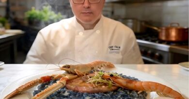 Chef Alex Ziccarelli in a professional kitchen presents squid ink pasta topped with large prawns.